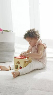 4k video of cute little girl with curly hair sitting on the floor playing with cube of wooden colorful pieces and shapes. montessori materials. concept development and learning in the childhood stage