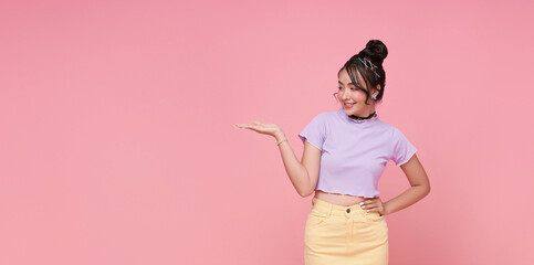 Smiling young asian teen girl looking and presenting showing place for your advertising text Isolated on pink copy space background.