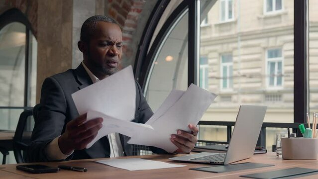 African American adult manager male guy in office ethnic businessman stressed puzzled angry furious mad man employer entrepreneur anger with papers paperwork business problem throw documents away sad