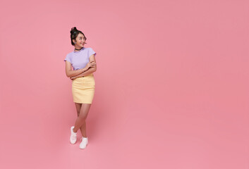 Happy asian teen woman standing with arms crossed and looking away isolated on pink copy space...
