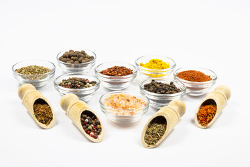 Assortment of spices in wooden spoons and glass bowls isolated on white background.