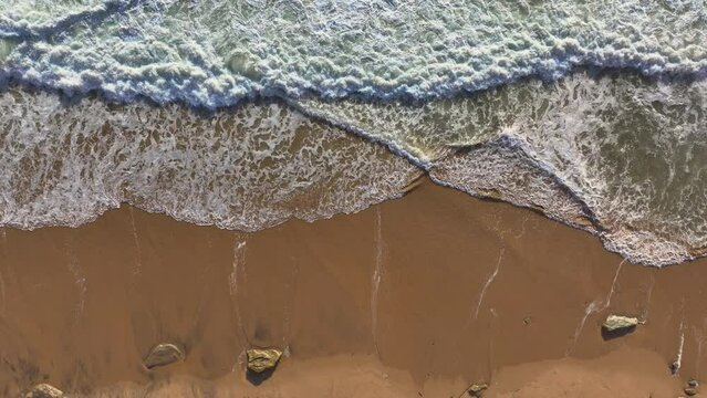 AERIAL TOP DOWN: Stunning patterns formed by waves spilling over wet sandy shore. Ocean waves gently lapping along an empty stretch of sandy beach. Beautiful Portuguese coastline by the Atlantic Ocean