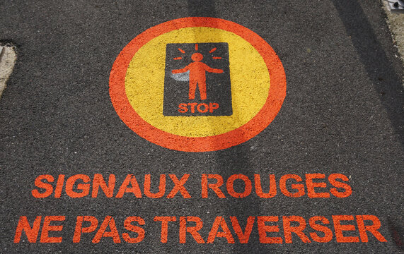 Sign painted on a sidewalk at a railroad crossing in France. French language warns pedestrians do not cross when the signal is red.