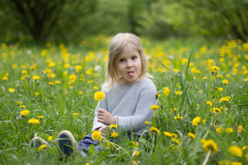 Little European funny girl 4 years old, beautiful, with long blond hair, fools around sitting on...