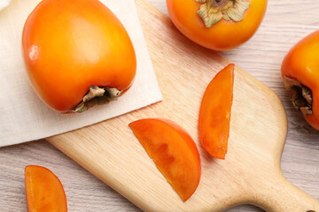 Delicious ripe persimmons on light wooden table, top view