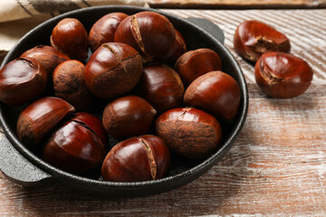 Fresh edible sweet chestnuts in frying pan on wooden table, closeup