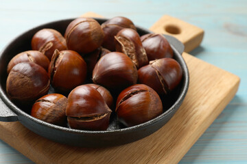 Fresh edible sweet chestnuts in frying pan on light blue wooden table, closeup