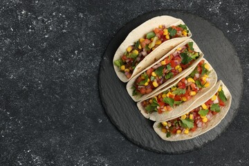 Tasty tacos with vegetables on black textured table, top view. Space for text
