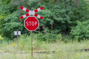 Stop sign and Saint Andrew s cross - railway crossing in the forest. A forest railway line among lush trees on a July afternoon. Road signs at a railway crossing.  - obrazy, fototapety, plakaty