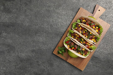 Delicious tacos with meat and vegetables on gray textured table, top view. Space for text