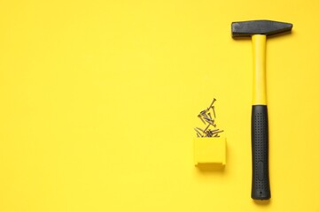 Hammer and metal nails on yellow background, top view. Space for text
