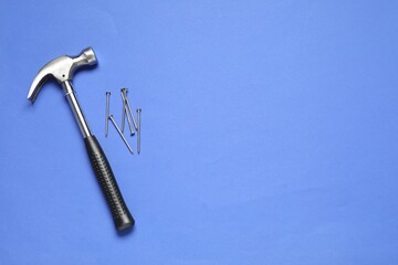 Hammer and metal nails on blue background, top view. Space for text