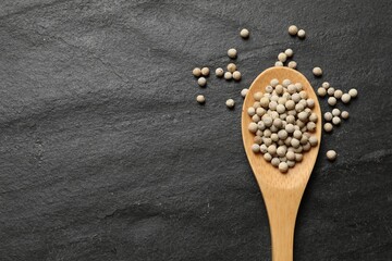Aromatic spice. White pepper in spoon on black table, top view. Space for text