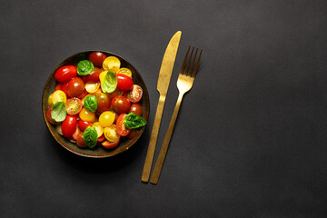 Bright juicy salad with colorful cherry tomatoes and aromatic basil leaves on black stone table top...
