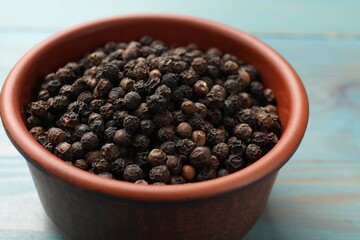 Aromatic spice. Black pepper in bowl on light blue wooden table, closeup