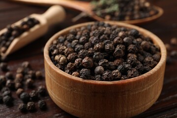 Aromatic spice. Black pepper in bowl and scoop on wooden table, closeup