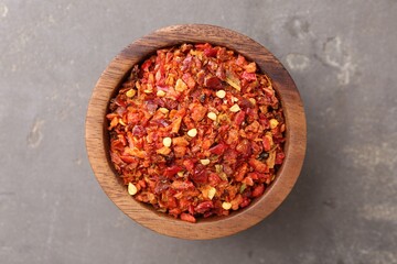 Chili pepper flakes in bowl on grey table, top view