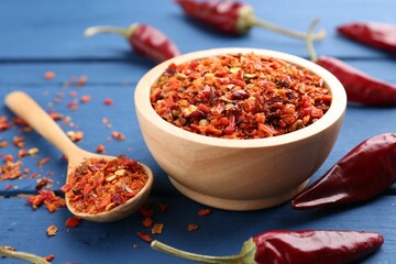 Chili pepper flakes and pods on blue wooden table, closeup