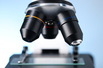 Modern microscope on light blue background, closeup view