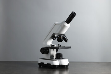 Modern medical microscope on grey table against light background