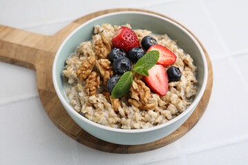 Tasty oatmeal with strawberries, blueberries and walnuts in bowl on white tiled table, closeup