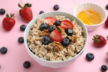 Tasty oatmeal with strawberries, blueberries and walnuts in bowl surrounded by fresh berries on pink background