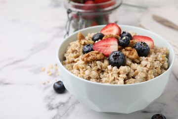 Tasty oatmeal with strawberries, blueberries and walnuts in bowl on white marble table, closeup. Space for text