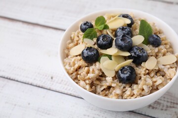Tasty oatmeal with blueberries, mint and almond petals in bowl on wooden table, closeup. Space for text