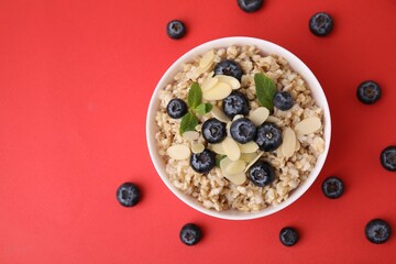 Tasty oatmeal with blueberries, mint and almond petals in bowl surrounded by fresh berries on red...