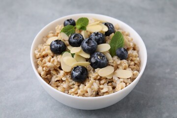 Tasty oatmeal with blueberries, mint and almond petals in bowl on grey table