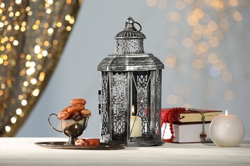 Arabic lantern, Quran, misbaha, candle and dates on white table against blurred lights