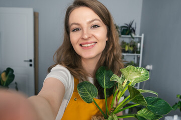 Beautiful girl gardener in yellow apron taking selfies with flower after transplanting.