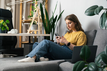 Girl talking on the phone while sitting on the sofa surrounded by indoor plants. Beautiful girl...