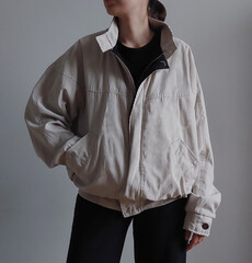 Woman wearing light vintage bomber jacket and black pants isolated on light background.