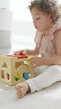 4k slow motion video of a cute little girl with curly hair sitting on the floor playing with a cube of colorful wooden pieces and shapes. montessori materials. concept development and learning in the 