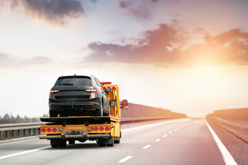 Roadside assistance. Tow truck transporting a broken car on a highway. Flatbed towing truck with a...