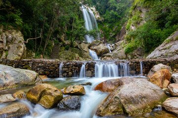 Waterfall cascading through rocky terrain surrounded by lush greenery and rocks.