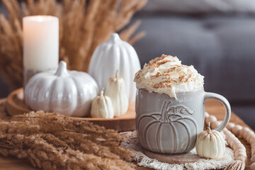 Obraz na płótnie Canvas A seasonal drink. Delicious pumpkin latte with whipped cream and cinnamon in a mug on a wooden table in the living room interior.Autumn decor in the house. Scandinavian style.