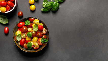 Bright juicy salad with colorful cherry tomatoes and aromatic basil leaves on black stone table top view. Healthy vegan food concept.