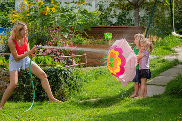 Summer day garden fun play of kids and mother with water hose
