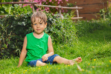 Child with green sleeveless shirt and blue shorts relax on lawn