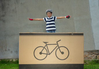Teen in bike helmet situated on big box displays bicycle emblem