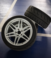 Detail of three sports car wheels stacked on the parking lot floor, white 6-spoke wheels with...
