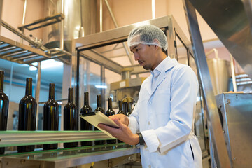 Winemaker working with digital tablet near line of conveyor during manufacturing in winery factory....