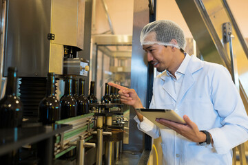 Winemaker working with digital tablet near line of conveyor during manufacturing in winery factory....