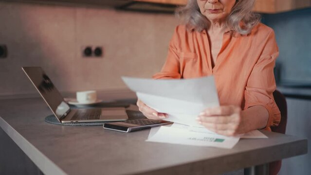 Senior woman holding energy bill and calculating expenses, paying bills online
