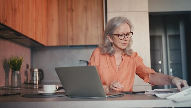 Senior businesswoman calculating budget, paying bills on laptop, doing taxes
