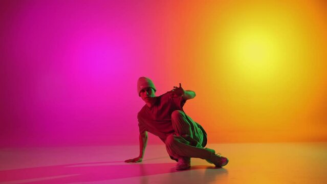 Young man, talented breakdancer dancing in motion in mixed neon light against gradient pink-yellow background. Concept of hobby, sport, creativity, fashion and style, motion, action. Ad
