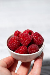 fresh raspberries in a white bowl in hand, vertical