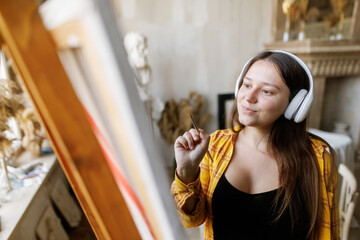 Moving paint brush artist works on abstract oil painting in creative modern studio. Girl with headphones listening to music. Abstract Modern Art.
